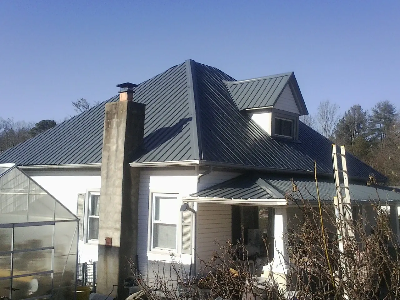 Dark blue standing seam metal roof on a white farmhouse with dormer — Slate & Tile Roof Repair by Roofing Brothers in Mendon