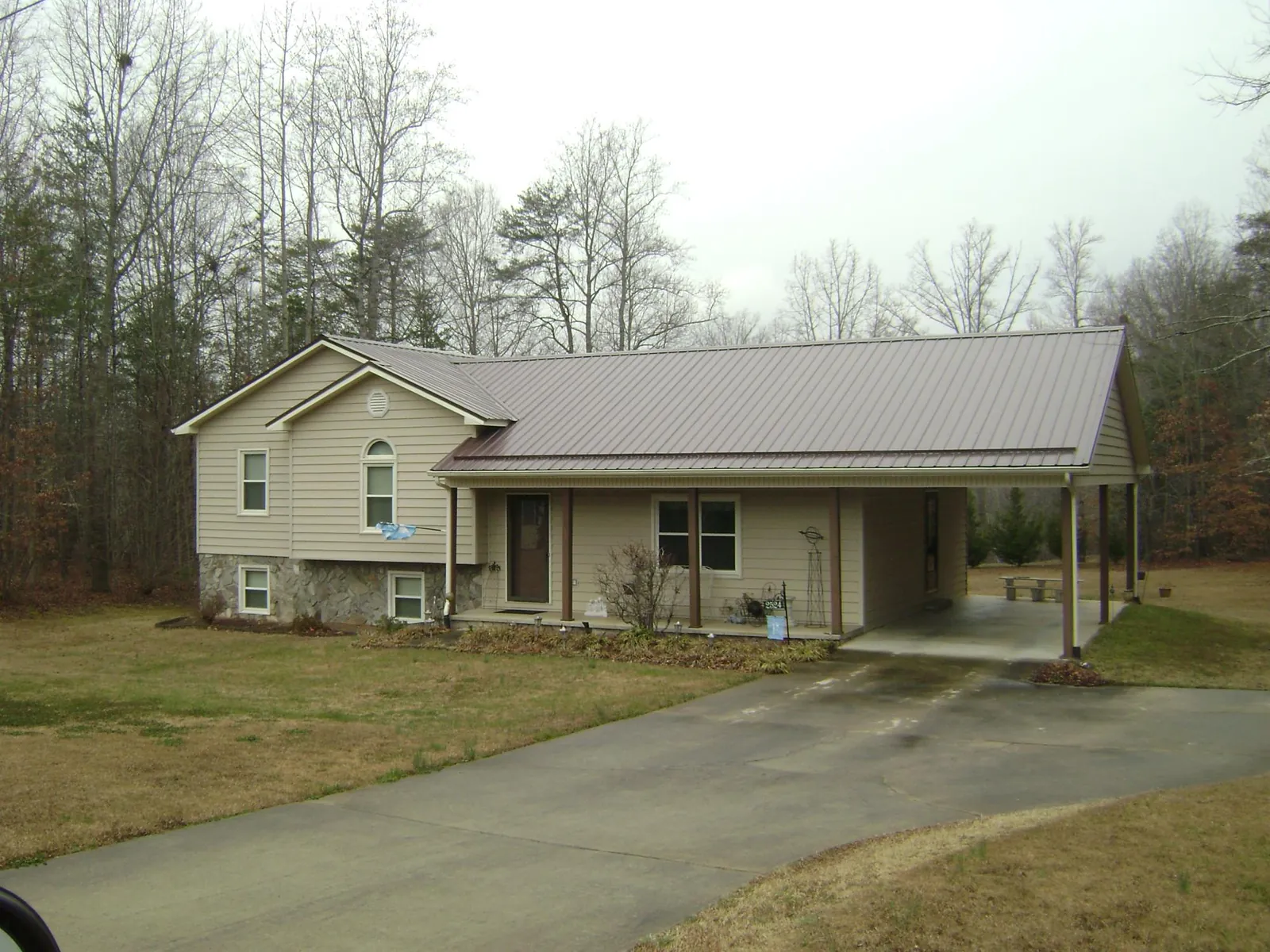 Brown metal roof on a tan split level home with an attached carport in Mendon