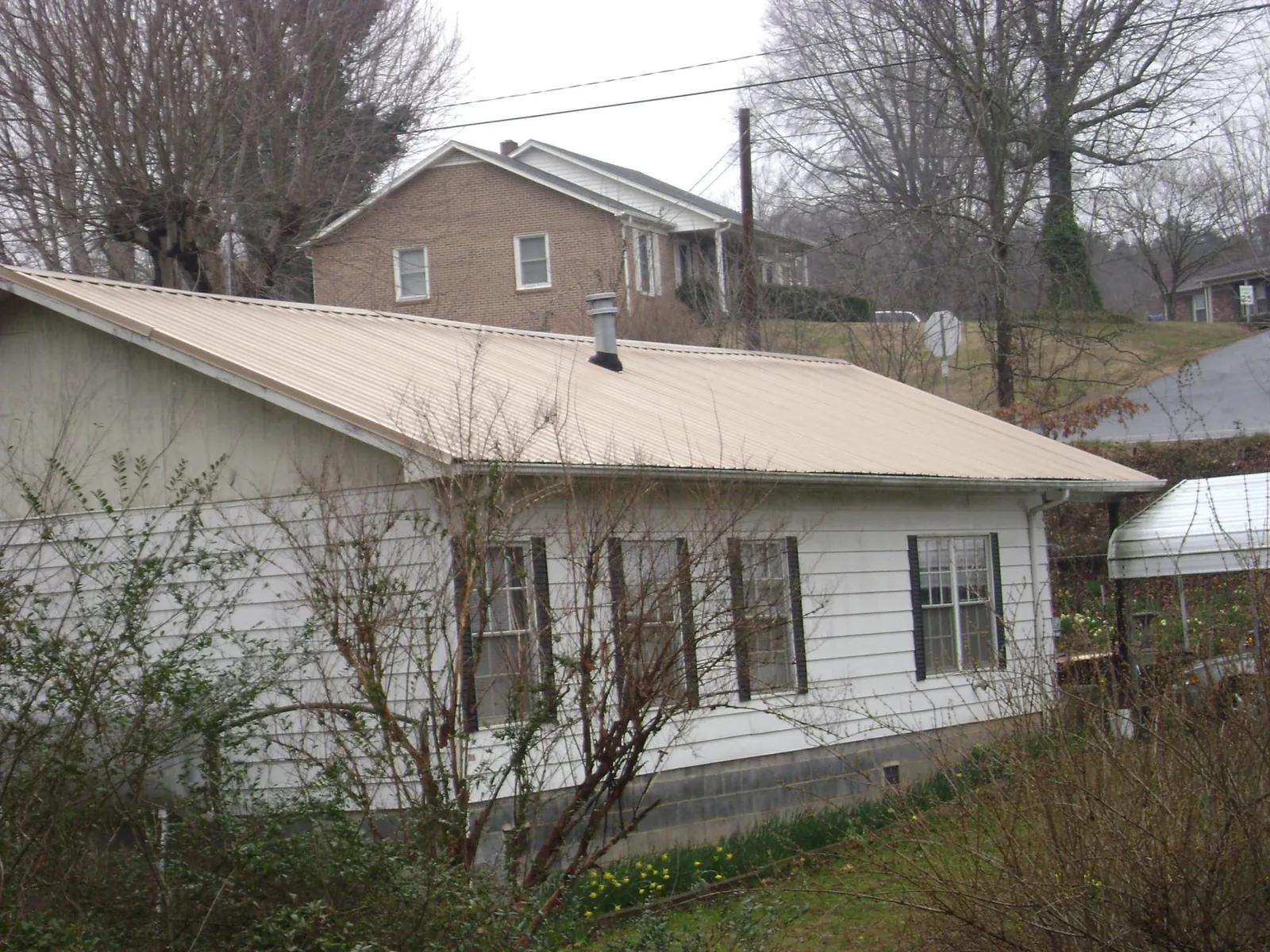 Tan metal roof on a white sided house set into a hillside — Commercial Roofing by Roofing Brothers in Mendon