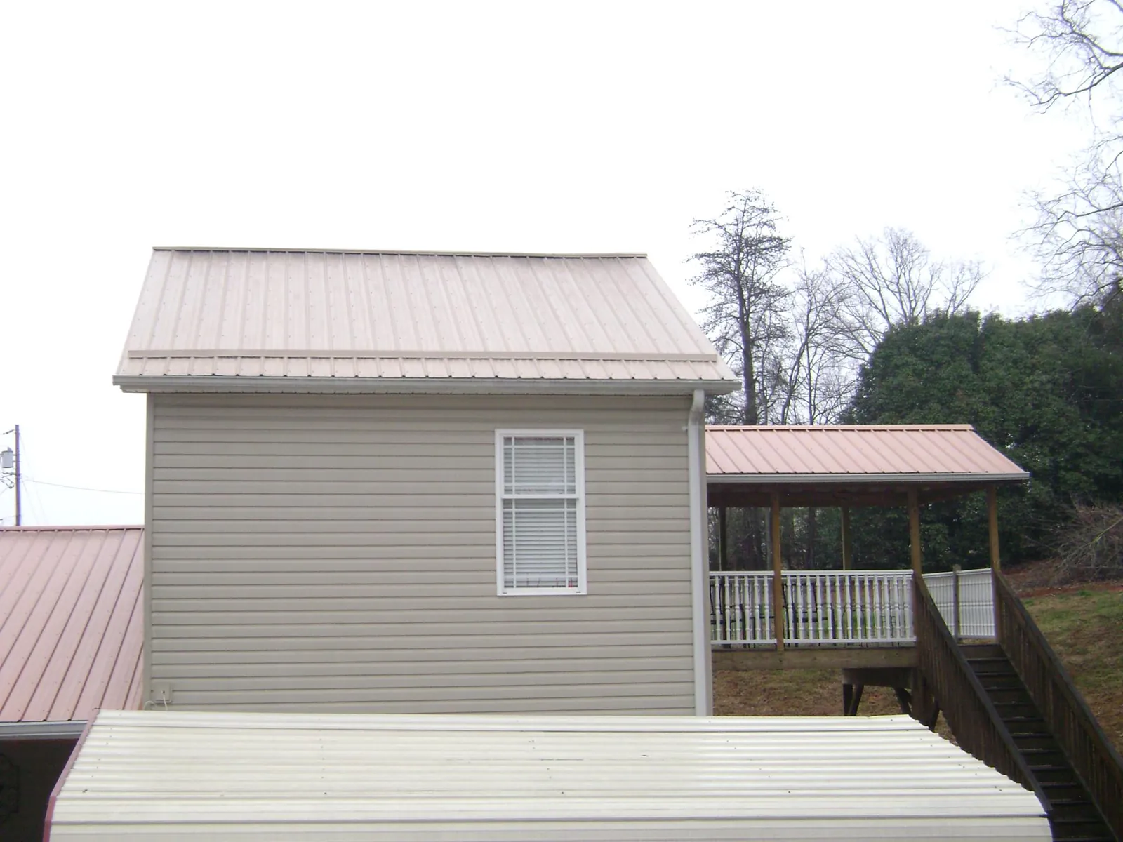 Tan metal roofs on a two story addition and attached porch, from a Roof Replacement job in Mendon